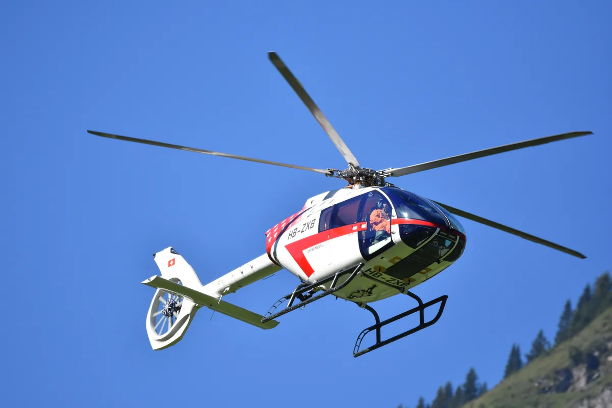 Ein weisser Helikopter mit rotem Streifen auf der Seite in der Luft.