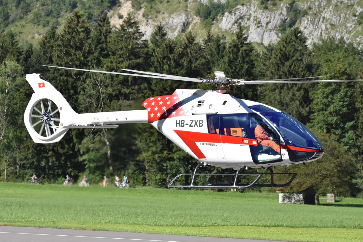 Ein weisser Helikopter mit rotem Streifen auf der Seite hebt ab.