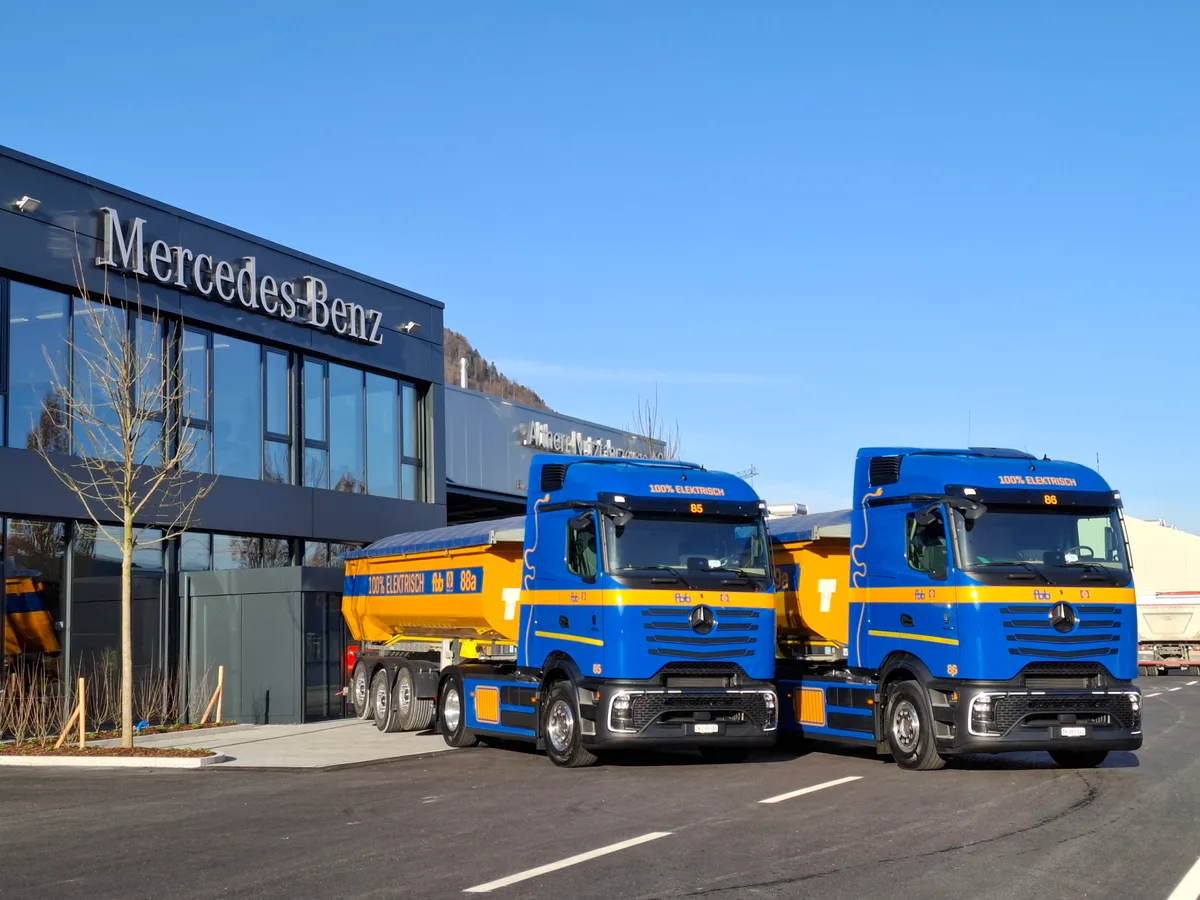 Zwei gelb-blaue Sattelschlepper der Firma FBB stehen vor einem Gebäude, das mit «Mercedes-Benz» angeschrieben ist.