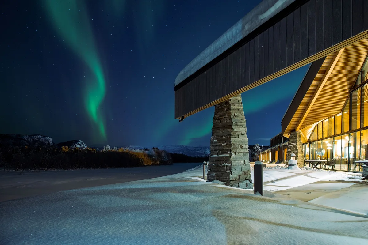 Das Eishotel in Alta (Norwegen) wird jedes Jahr neu gebaut und unter ein neues Motto gestellt. Der Eingang zum Eishotel in Alta. Man sieht eine Holz-Glas-Konstruktion und ein grünes Polarlicht.