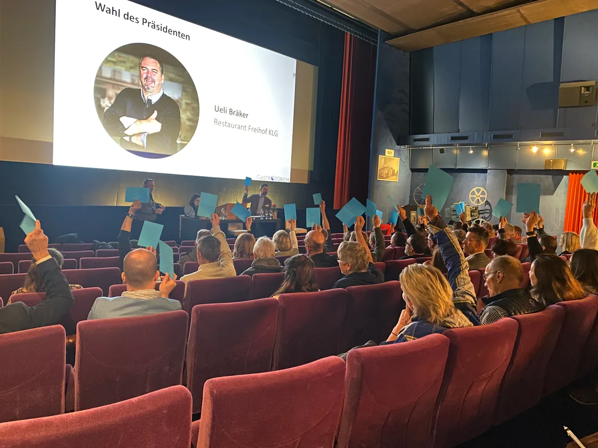 Menschen sitzen im Kino Palace in Wetzikon und halten blaue Stimmkarten in die Höhe.