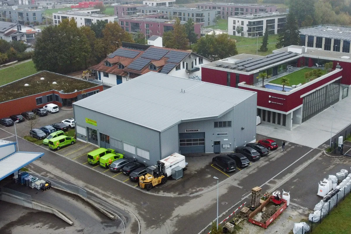 Luftaufnahme einer Gewerbehalle in Mönchaltorf. Man sieht eine graue Halle, rundherum parken Autos.