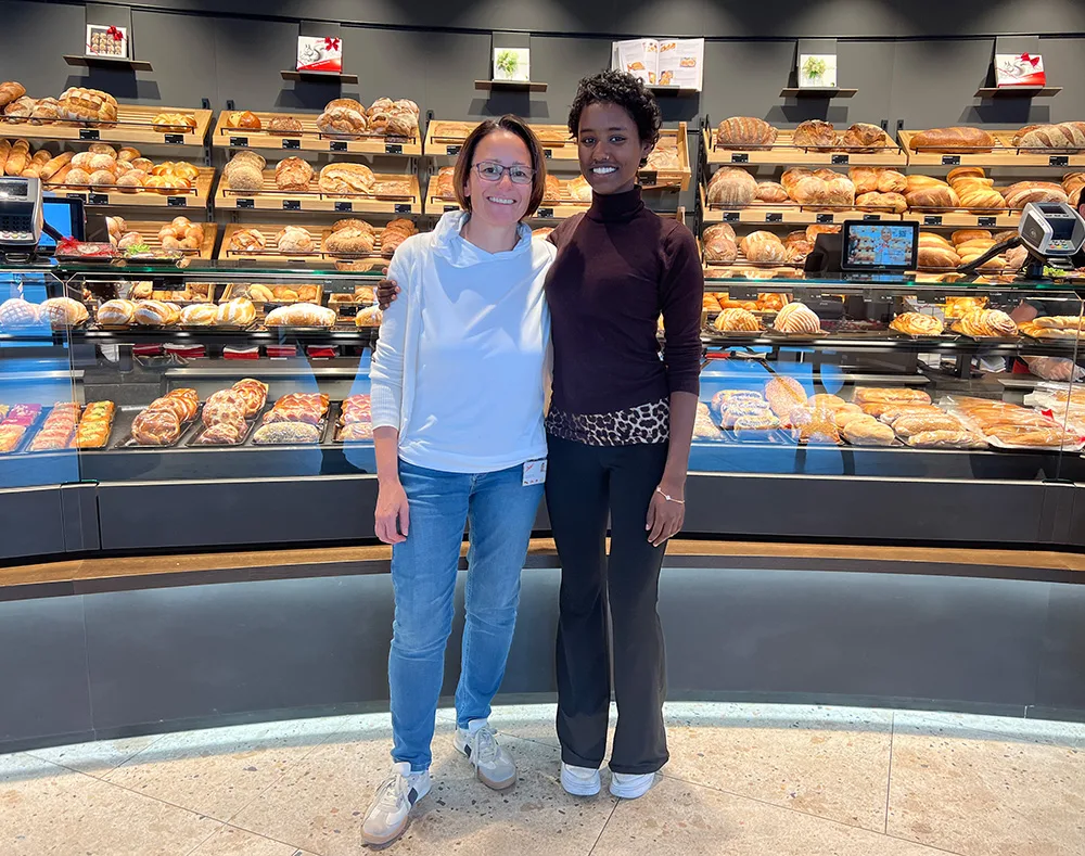 Zwei Frauen stehen in einer Bäckerei. Im Hintergrund die  Verkaufstheke mit vielen Broten.