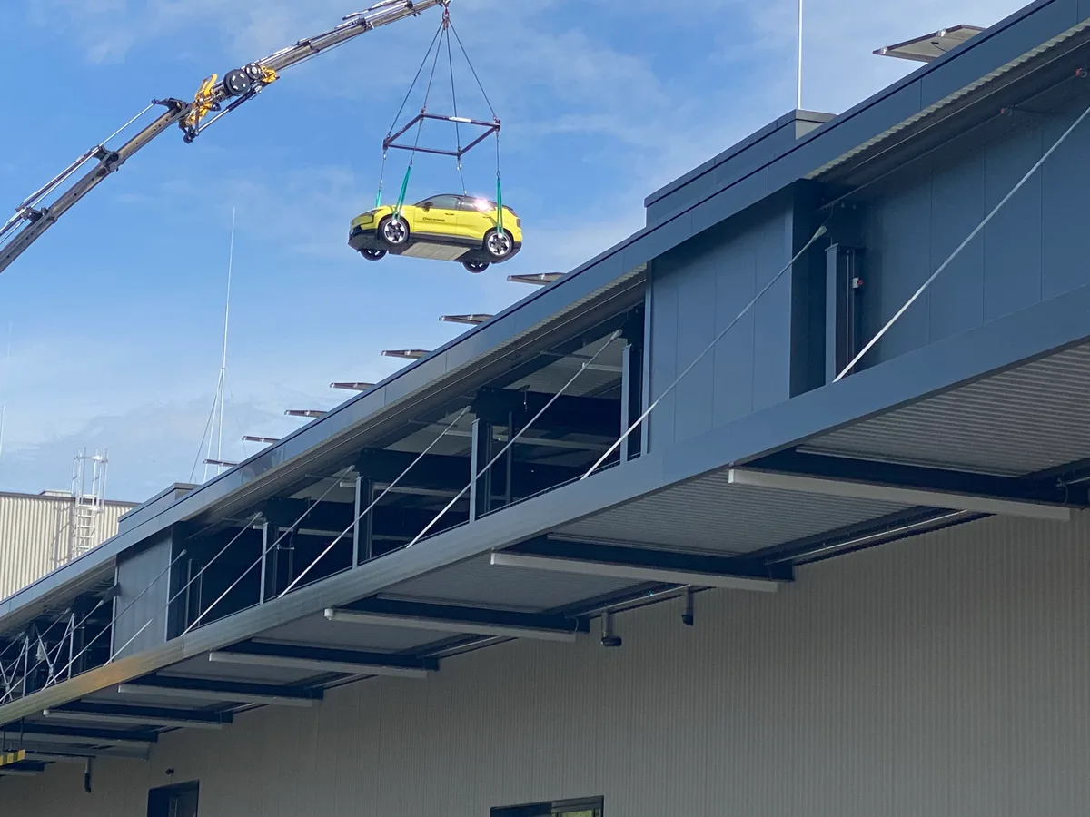 Ein gelber Volvo schwebt an einem Kran über einem Gebäude.