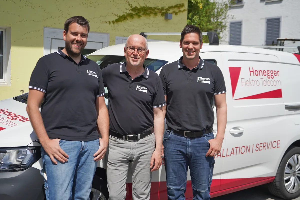 Simon (links) und Dominik (rechts) Honegger nahmen die Firmenübernahme von Walter Honegger zum Anlass, den Auftritt des Unternehmens sanft zu erneuern. Drei Männer stehen vor einem weissen Lieferwagen, der mit Honegger Elektro Telecom AG beschriftet ist.