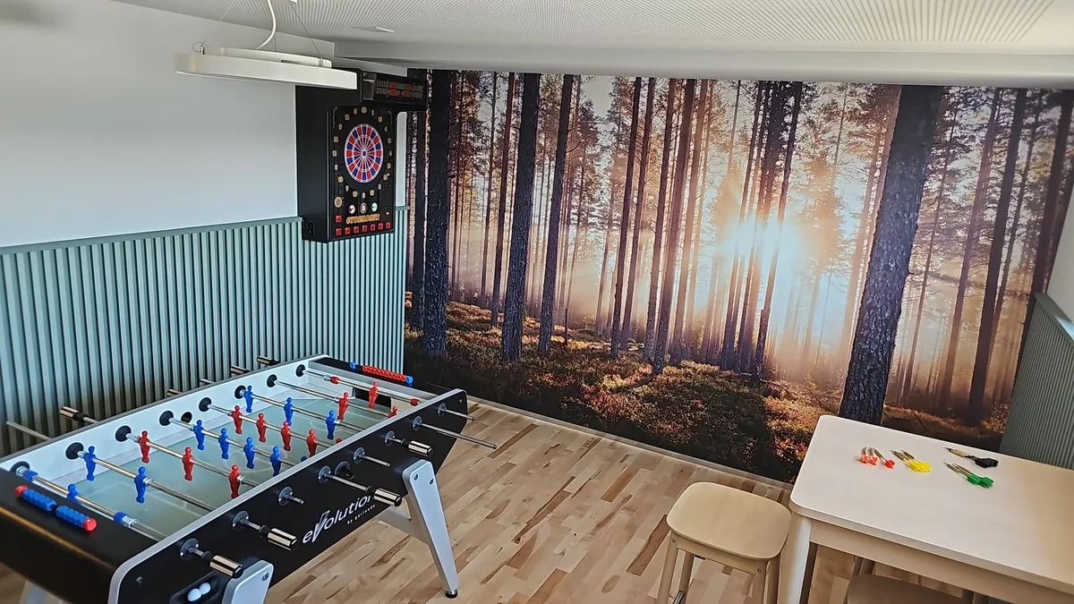 Der Aufenthaltsraum der Schaub Maler AG in Wetzikon. Man sieht einen Tisch mit Spielkarten, einen Tischfussballkasten und eine Tapete mit Bäumen, durch die die Sonne scheint.
