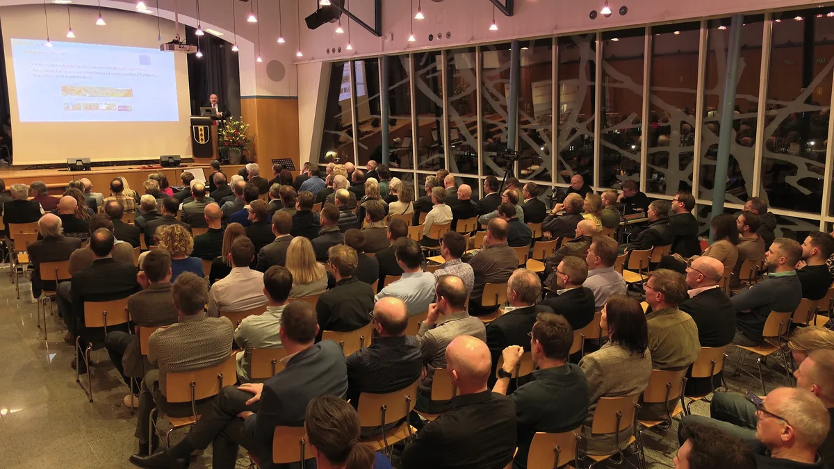 Menschen sitzen in einem Saal und hören ein Referat.