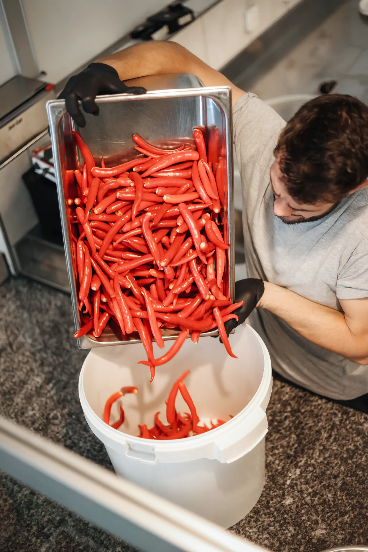 Ein Mann leert einen Metallbehälter voller Peperoncini in einen kleineren Plastikeimer.