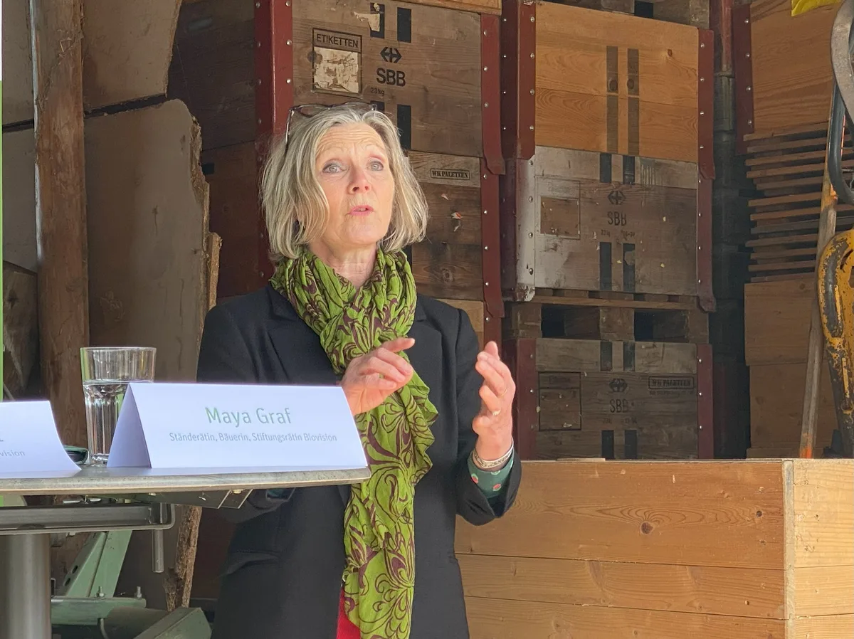 Ständerätin Maya Graf setzt sich für eine nachhaltigere Landwirtschaft ein. Maya Graf, Ständerätin und Biobäuerin, referiert hinter einen Stehtisch. Sie trägt einen grünen Schal über der dunklen Jacke.