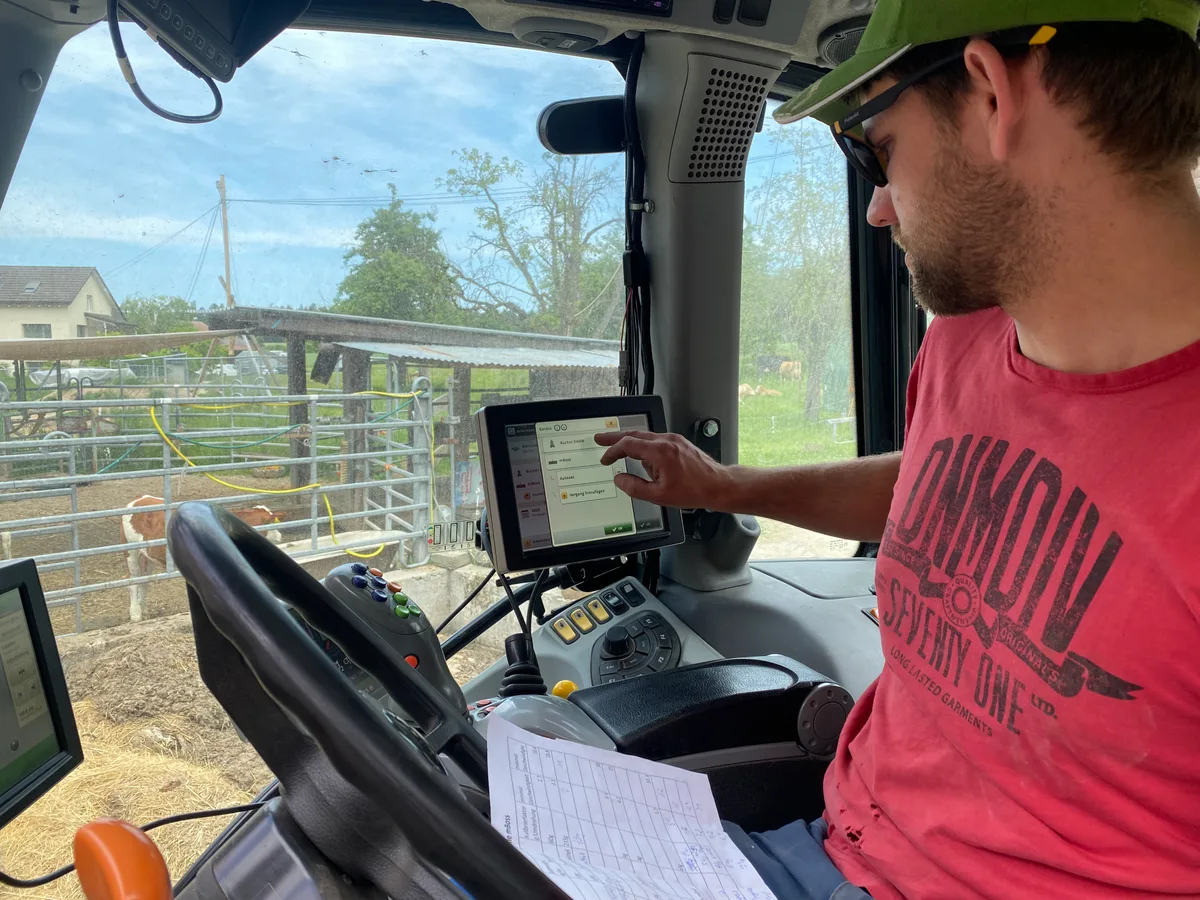 Benjamin Denzler programmiert das GPS. Der Traktor fährt zentimetergenau über das Feld. Landwirt Benjamin Denzler sitzt in seinem Traktor und programmiert den GPS-Sender.