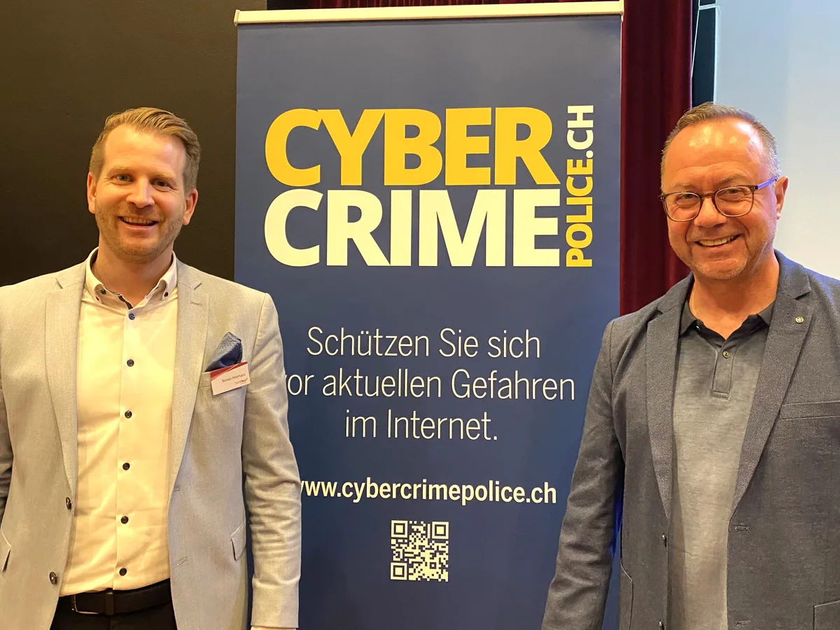 Zwei Männer stehen vor einem Plakat mit der Aufschrift Cybercrimepolice.ch.