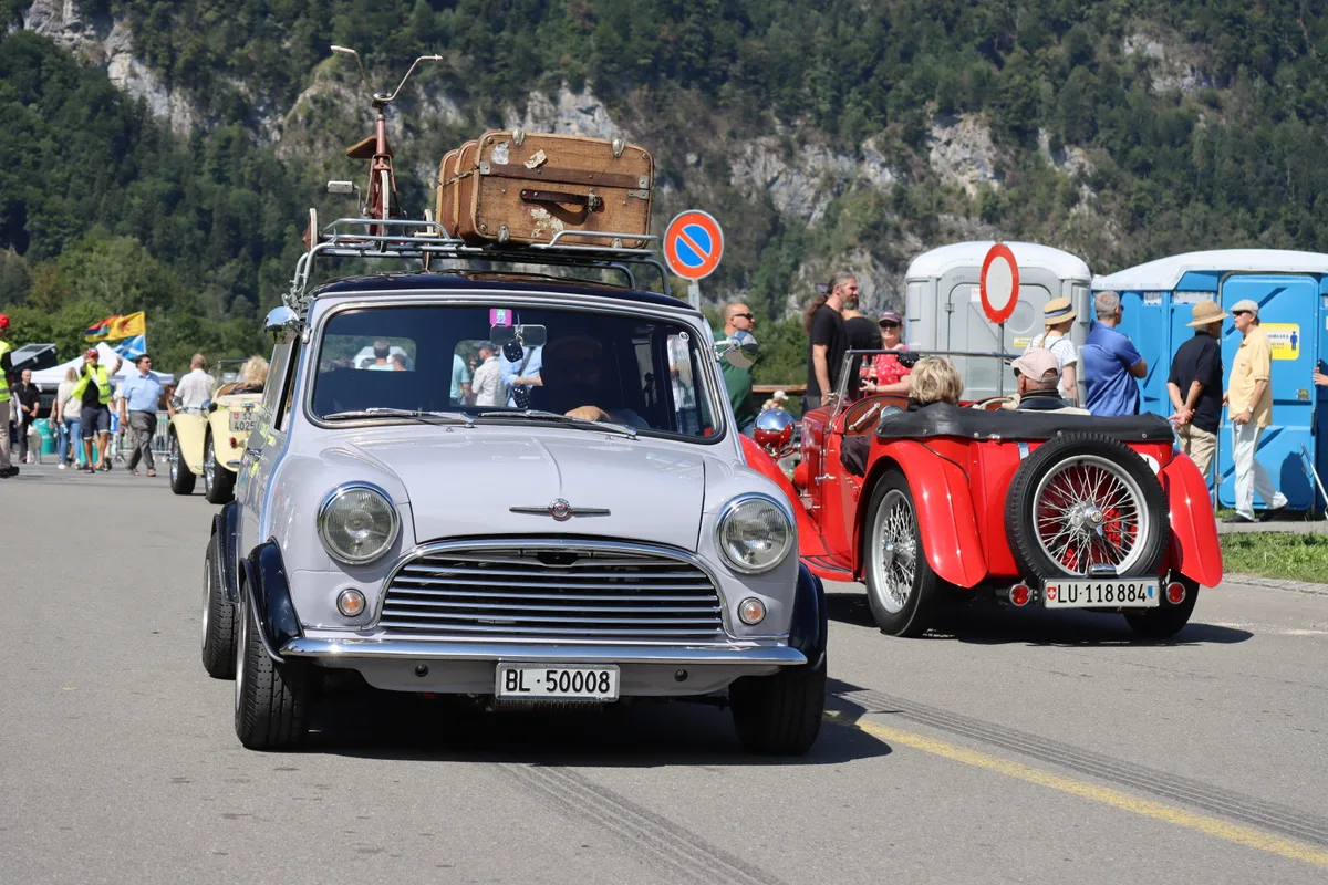 Ein Mini Cooper mit Dachträger. Darauf ein grosser Koffer und ein Dreirad.