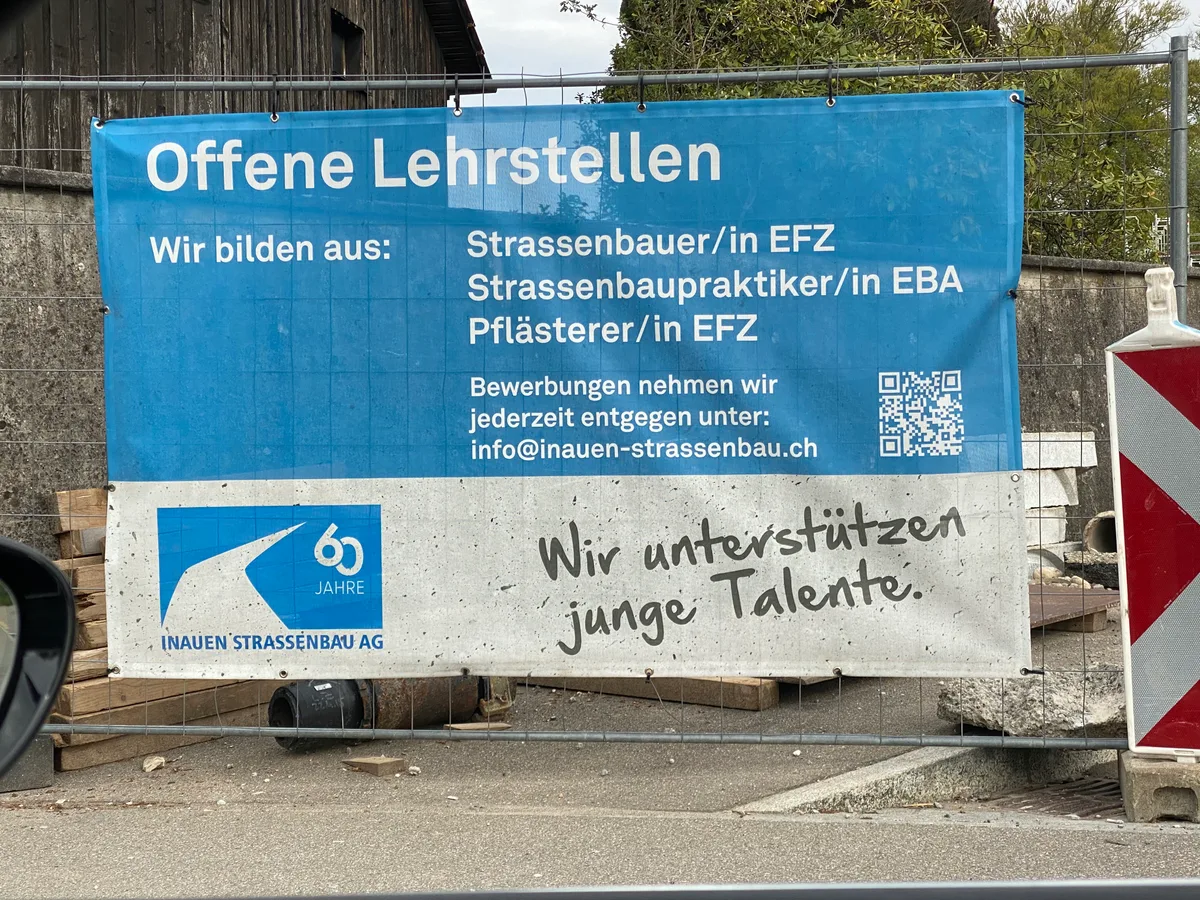 Offene Lehrstellen: Die Inauen Strassenbau AG sucht auch mittels Plakaten nach Nachwuchskräften. An einer Baustelle hängt ein Plakat der Inauen Strassenbau AG, auf dem Lernende gesucht werden.