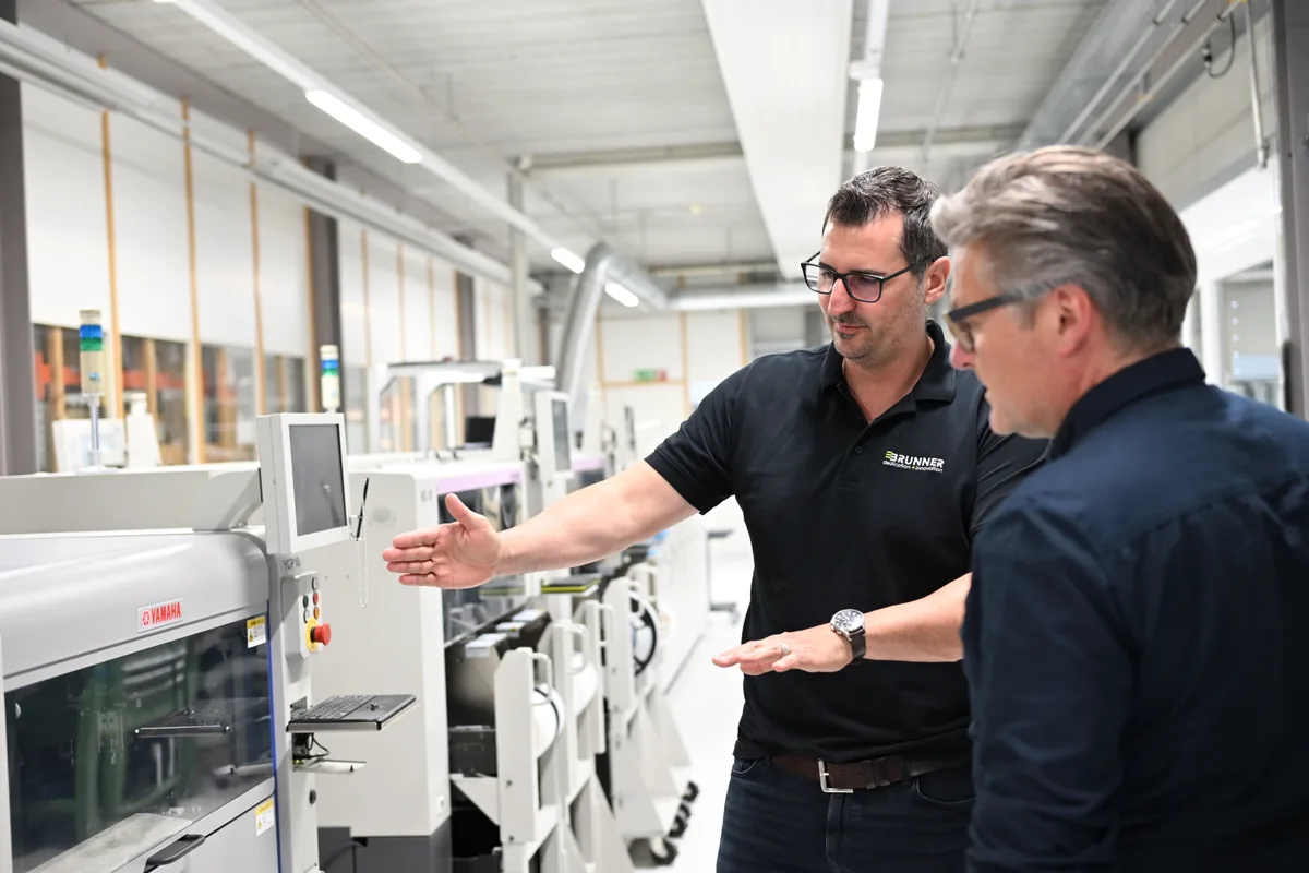 Eine Reihe von Hightech-Geräten, die zur Produktion von Halbleiterplatten eingesetzt werden. Davor zwei diskutierende Männer.