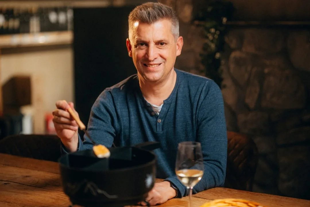 Jonny Billeter möchte mit seinem viergeteilten Fondue-Caquelon wachsen. Jonny Billeter sitzt an einem Tisch hinter einem Fondue-Caquelon. In seiner rechten Hand hält er eine Gabel.