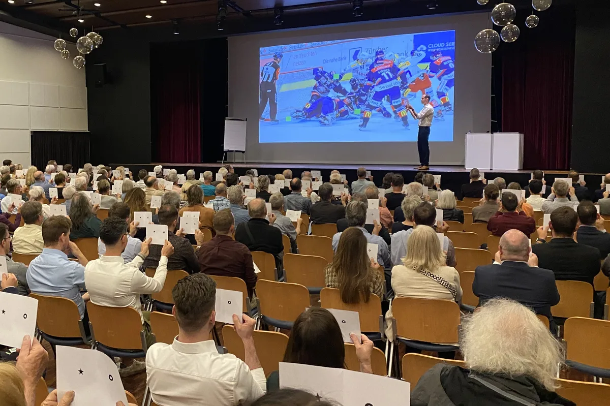 Menschen im Stadthofsaal halten weisse Zettel in die Höhe.