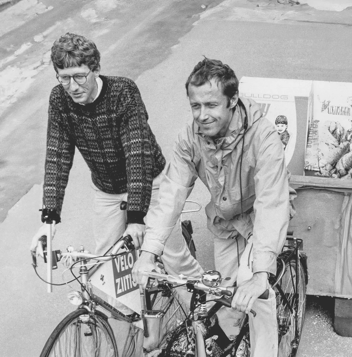 Schwarz-Weiss-Foto von zwei Männern, die mit ihren Velos einen Anhänger ziehen.
