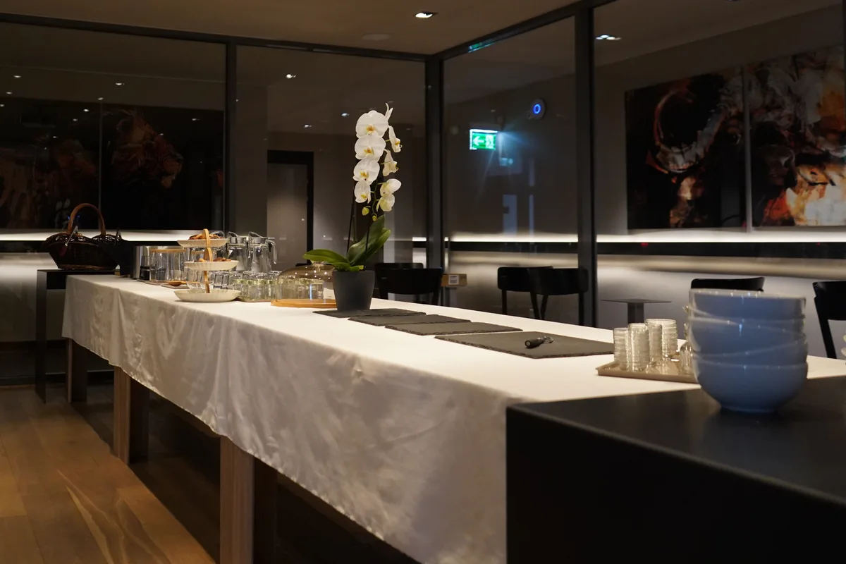 Ein langer, weiss gedeckter Tisch mit Gläsern und Karaffen. In einer Blumenvase steht eine Orchidee.