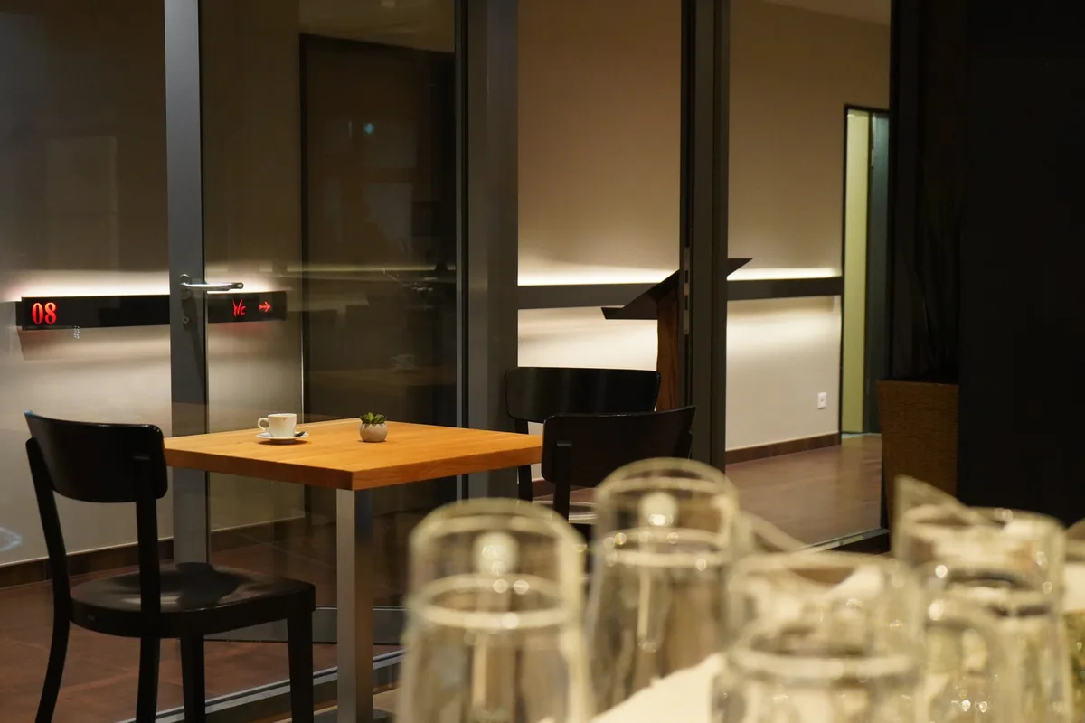 Ein kleiner Holztisch mit schwarzen Stühlen. Unscharf im Vordergrund gläserne Karaffen.