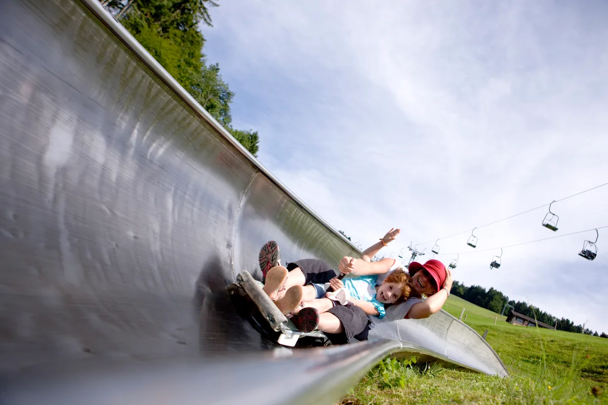 Eine Frau und ein Kind fahren mit einem Rodel die Sommerrodelbahn am Atzmännig hinunter.