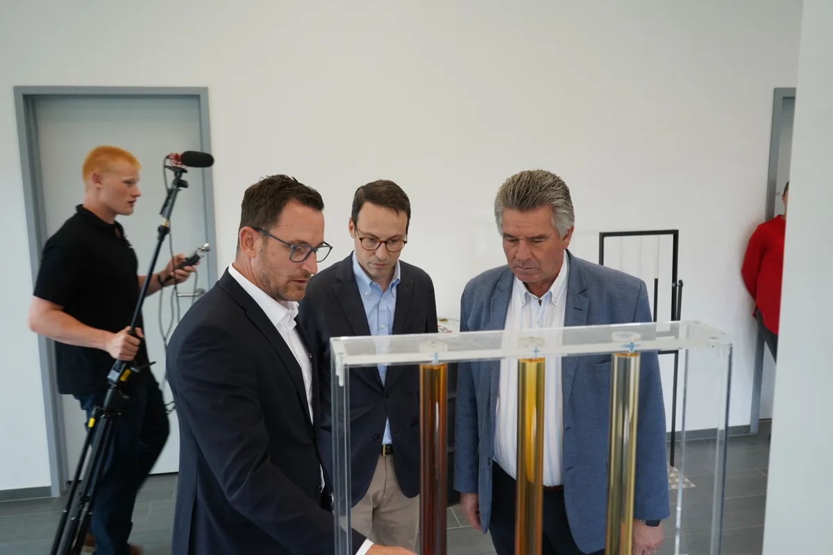 Besuch des stv. Umweltministers von Uruguay bei Roxor in Madetswil. Drei Männer stehen hinter Rohren mit verschiedenfarbenen Ölen.