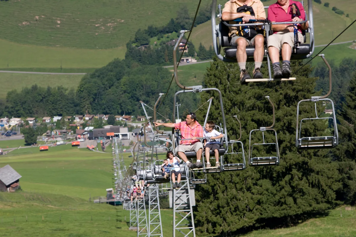 Menschen sitzen auf einer Sesselbahn. Sommeraufnahme.