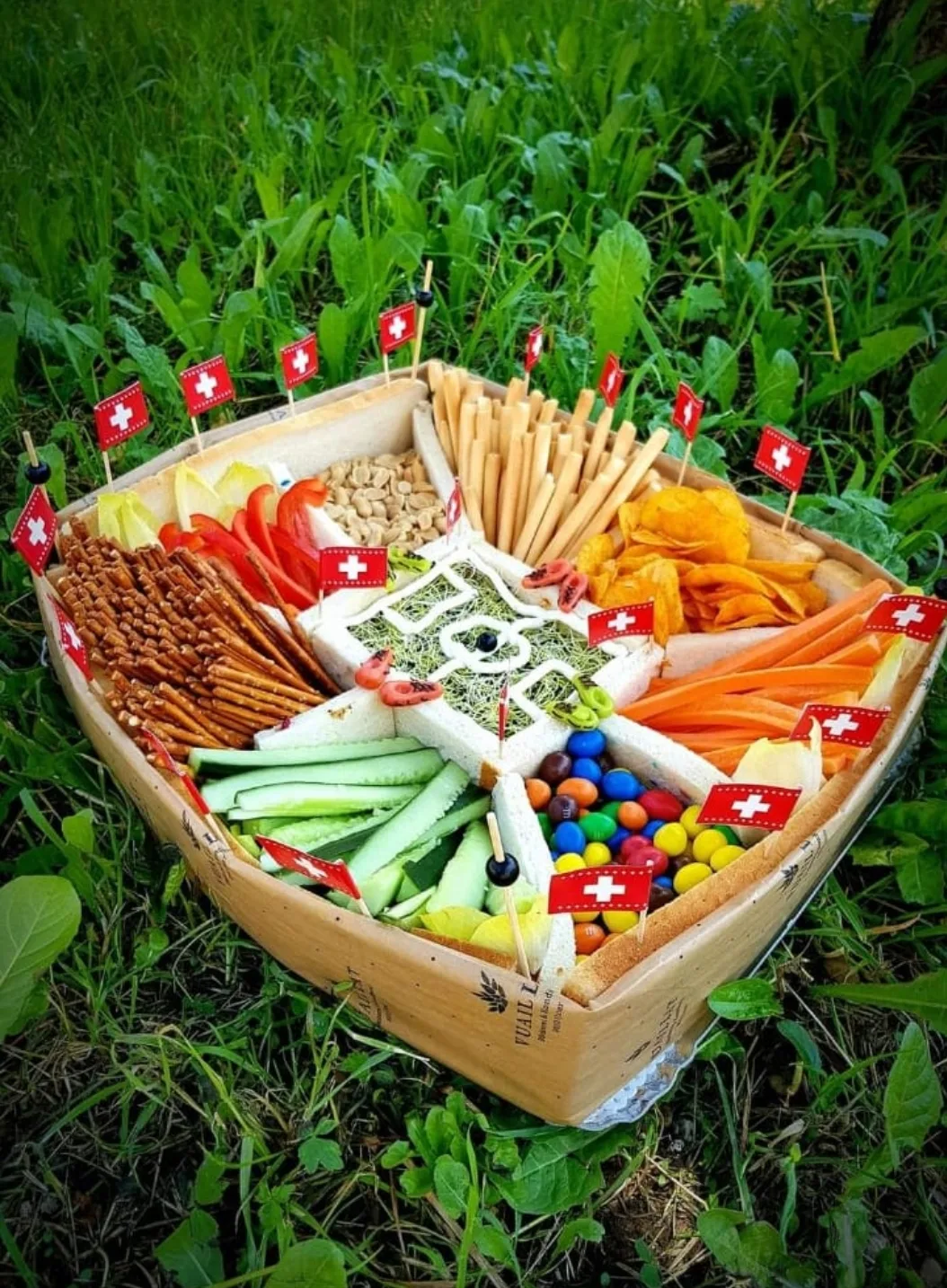 Ein Fussballstadion aus Brot, die Zuschauerränge sind Snacks wie Erdnüsse, Salzstangen, Smarties und Gemüsesticks. Im Zentrum als Spielfeld ein Dip.