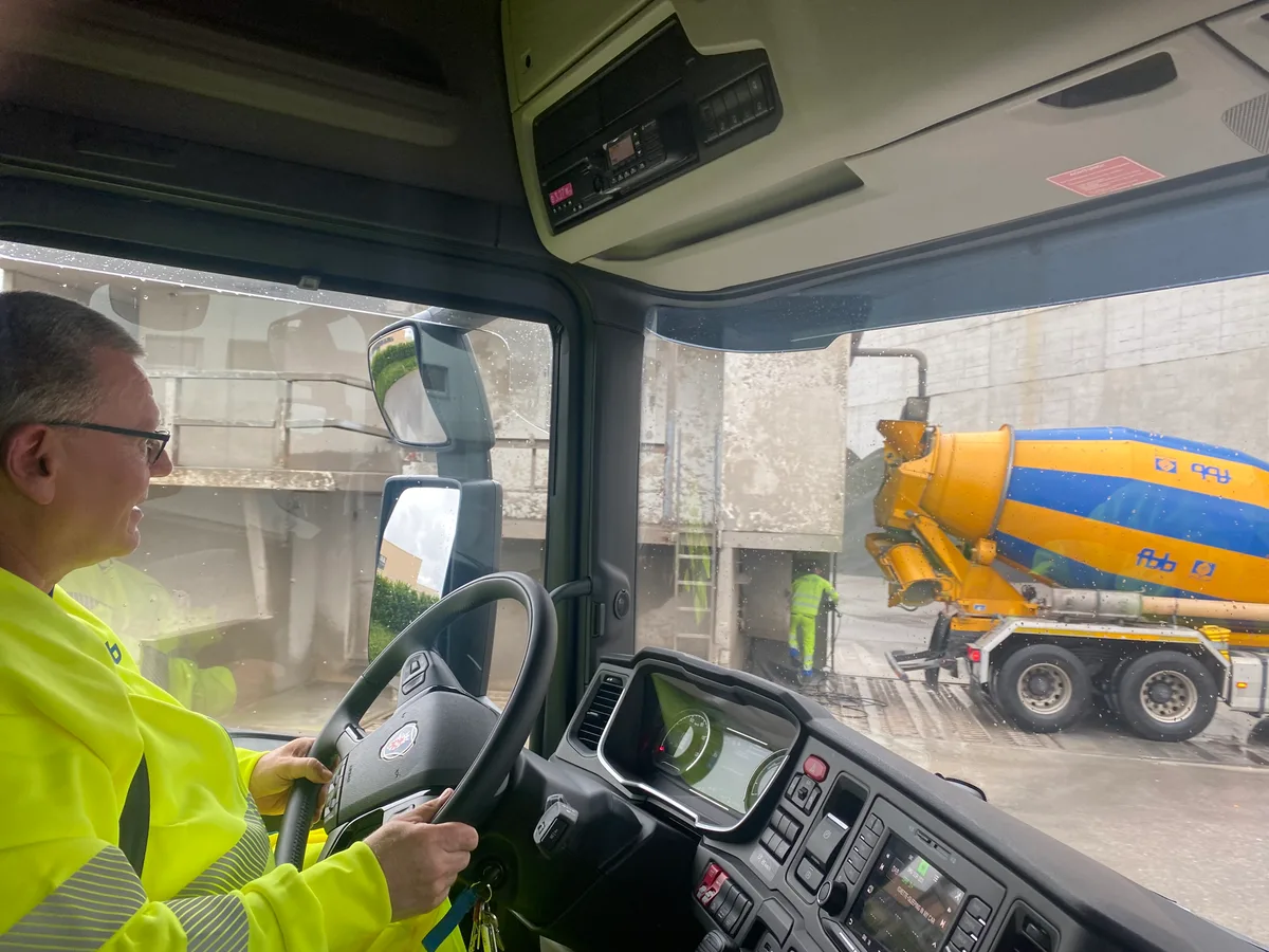 Ein Lkw-Chauffeur hinter dem Steuer seines Elektrolastwagens. Er trägt leuchtend gelbe Arbeitskleidung.