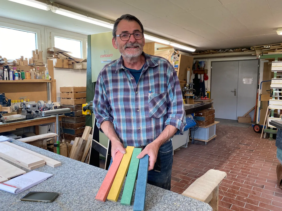 Ein Schreiner steht in seiner Werkstatt und hält farbige Holzlatten in seinen Händen.