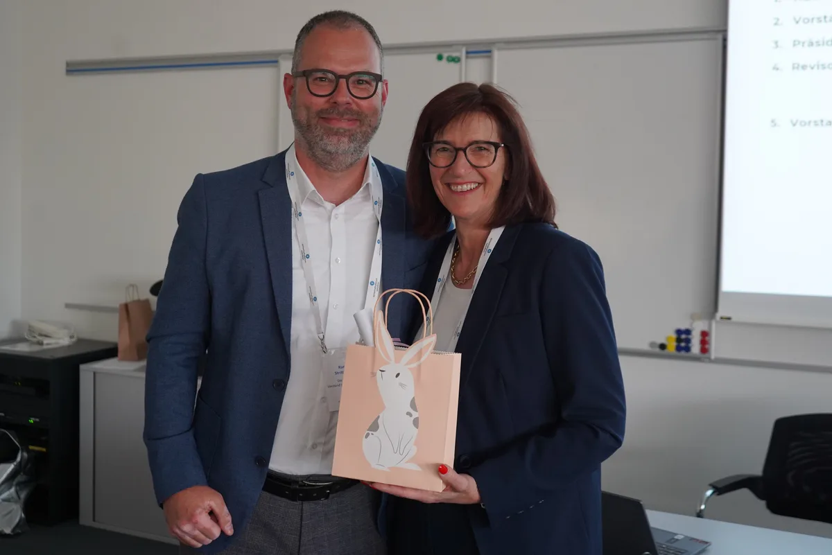 Ein Mann und eine Frau lächeln in die Kamera. Sie hält eine Papiertasche mit einem aufgedruckten Osterhasen.