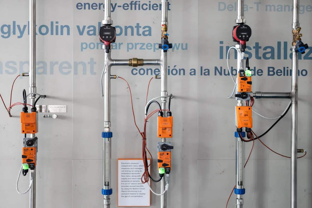 Blick in den Showroom von Belimo in Hinwil. Man sieht Rohre, an denen orangefarbene Mess- und Steuergeräte angebracht sind.