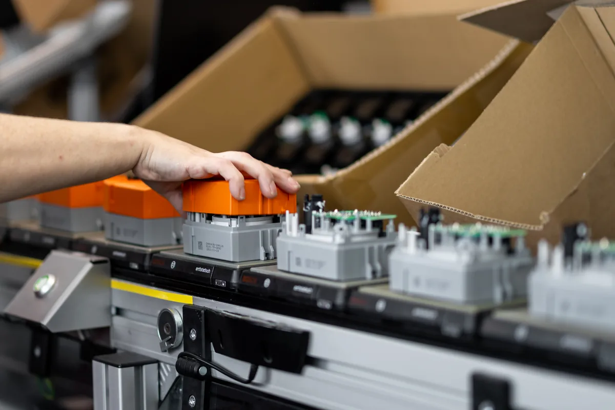 Produktion von Belimo in Hinwil. Ein Förderband mit grau-orangen Boxen.