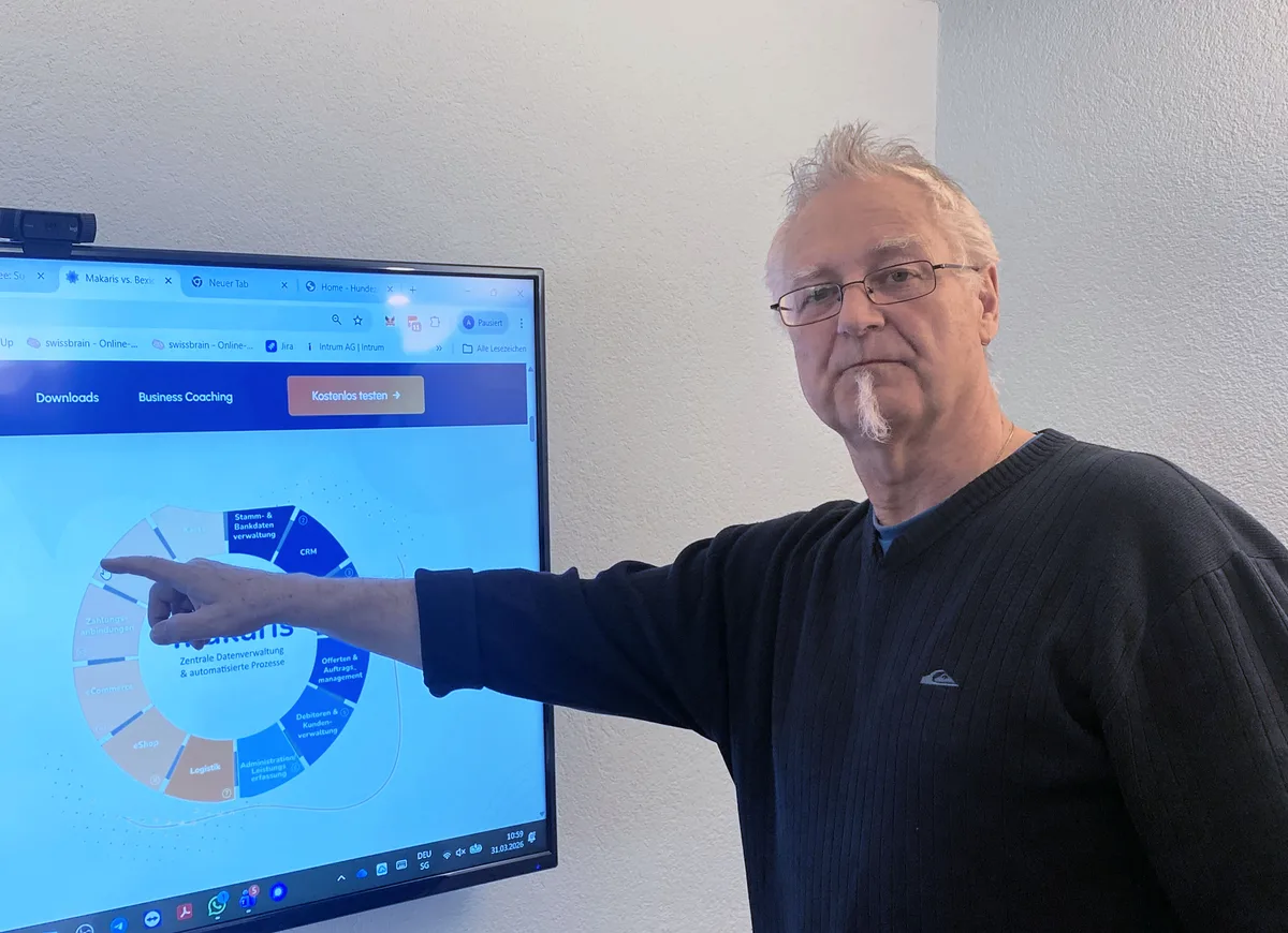 Porträt von André A. Zibung. Ein Mann mit weissem Haar und weissem Spitzbart zeigt auf einen Bildschirm.