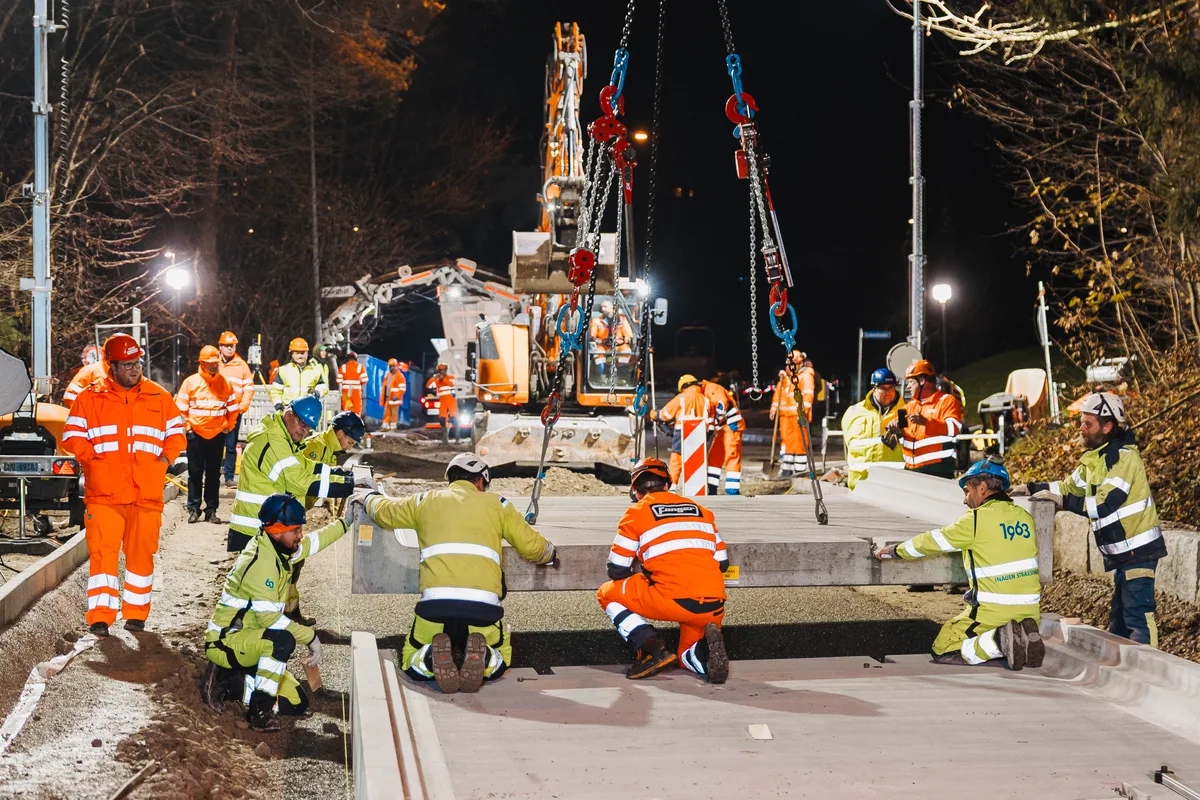 Patentiertes System: Dank vorgefertigten Betonelementen ist eine Bushaltestelle in wenigen Stunden saniert. Bauarbeiter in gelber und oranger Schutzkleidung montieren eine vorgefertigte Betonplatte.