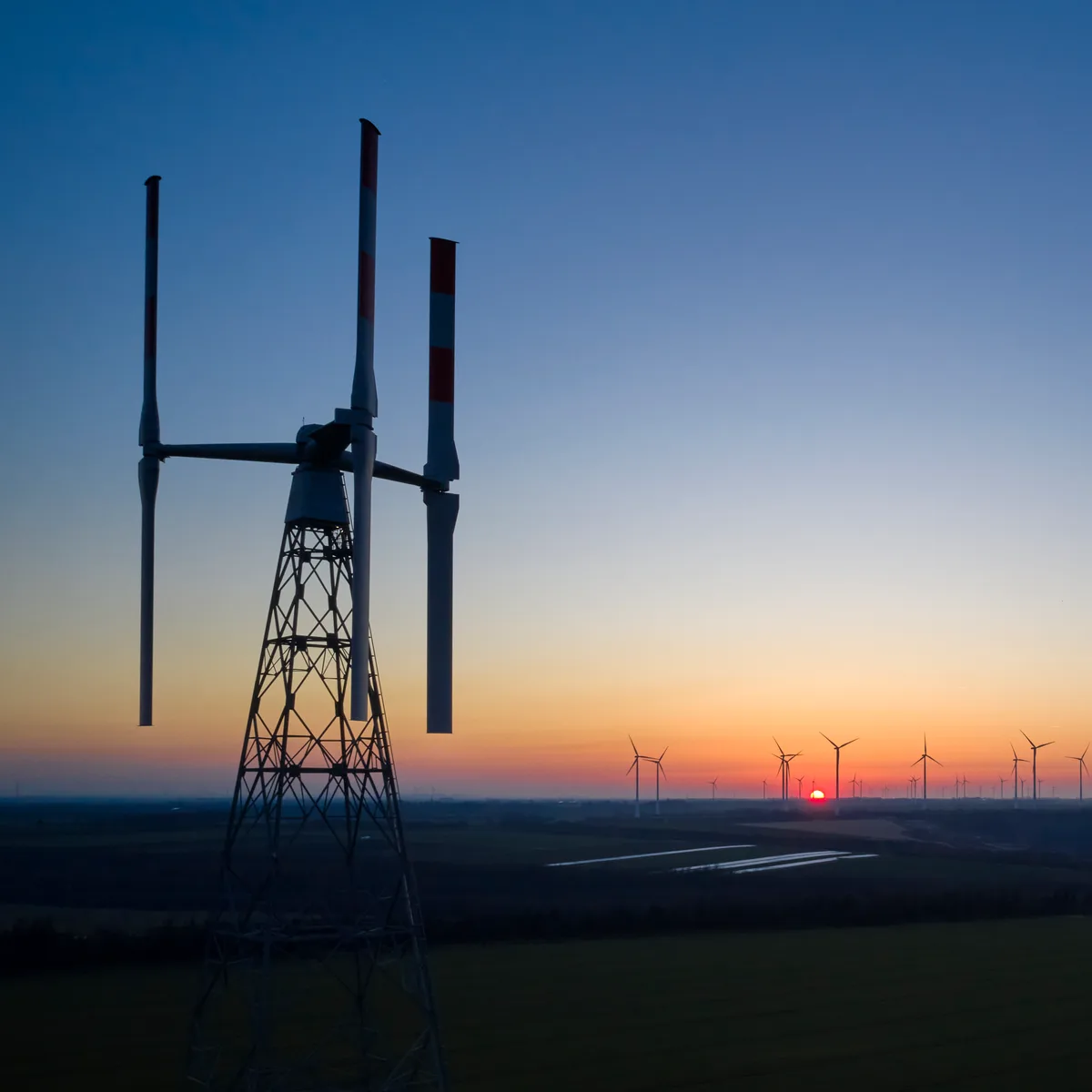 Eine vertikale Windturbine der Agile Wind Power AG. Die Testanlage steht in Grevenbroich (Deutschland). Man sieht einen Mast mit drei vertikal angebrachten Turbinen in der Morgendämmerung.
