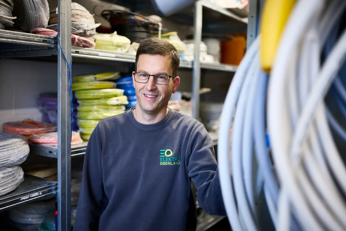 Ein Mann in blauem Pullover steht in einem Lagerraum mit vielen Kabelschläuchen.