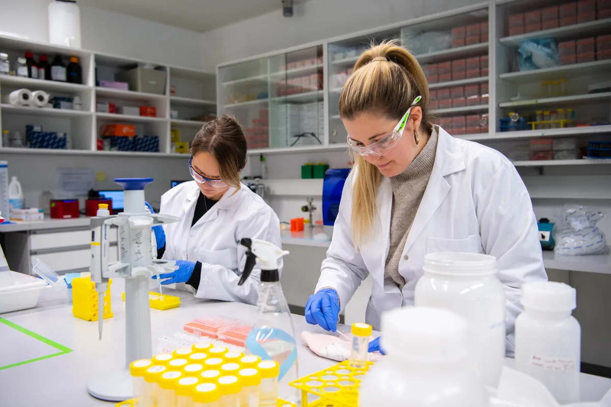Zwei Frauen in weissen Mänteln und mit Schutzbrillen in einem Labor.