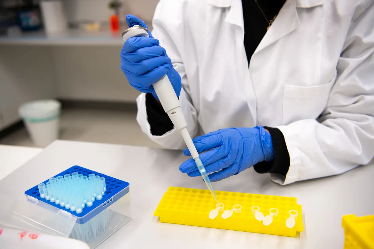 Eine Laborantin füllt eine klare Flüssigkeit in kleine Plastikbehälter.