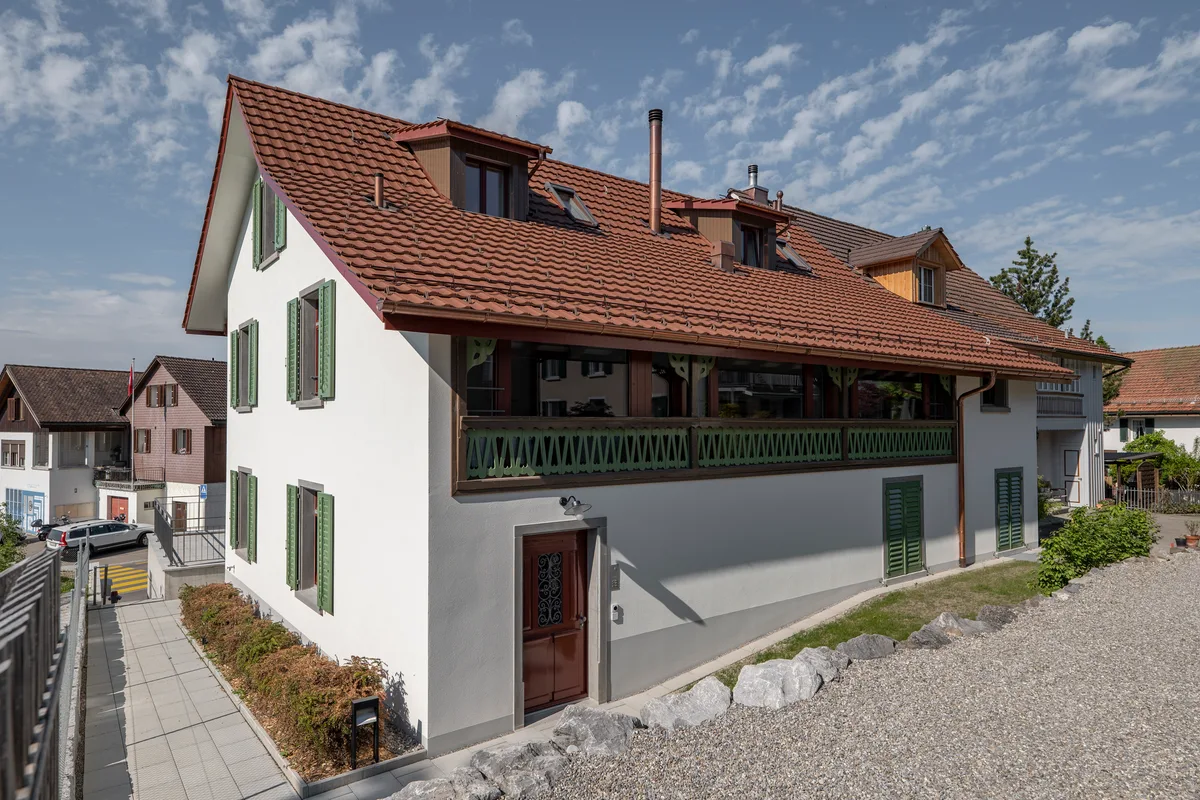 Aussenansicht der Sennerei Adetswil. Ein zweistöckiges, weisses Haus mit Satteldach und Holzbalkon.