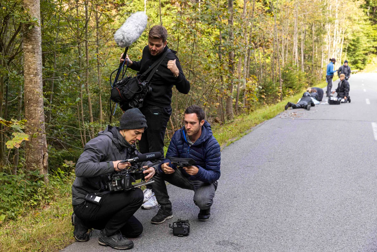 Die beiden Kameramänner Sebastian Klinger (links) und Janis Wolf am Set des Films «Sew Torn – Fäden des Verbrechens». Eine Filmcrew dreht eine Szene am Strassenrand.