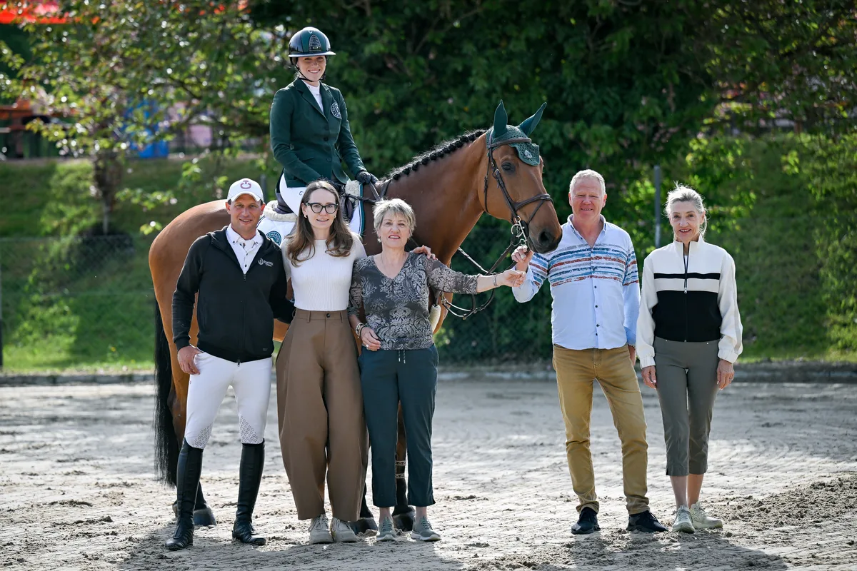 Eine Reiterin posiert auf ihrem Pferd mit ihrem Team.