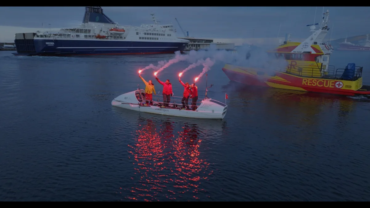 Die vier Extremruderer feiern ihre Einfahrt in den Hafen von Torshavn mit traditionellen Fackeln. Auf einem Ruderboot stehen vier Personen mit brennenden Fackeln.
