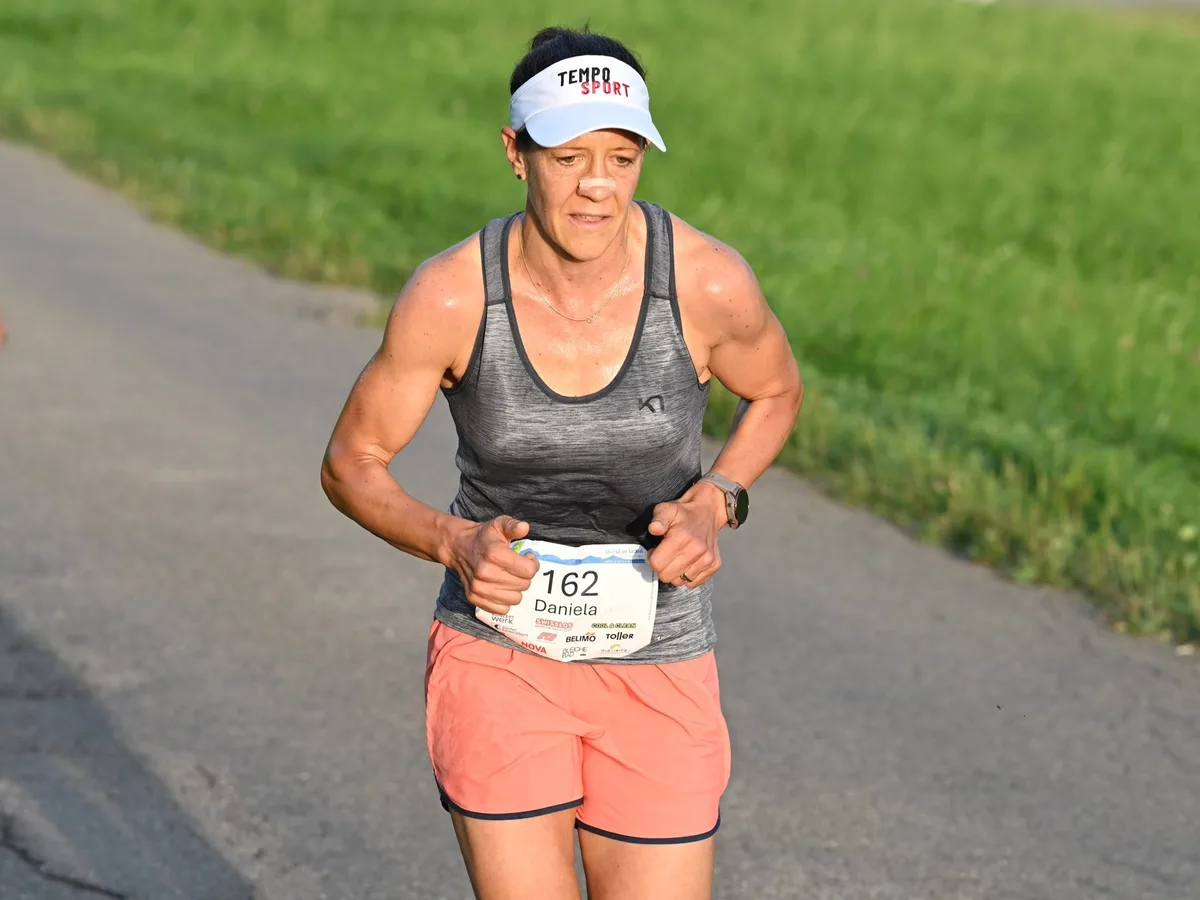 Ein Läuferin mit Dächlikappe auf einer Bergstrasse