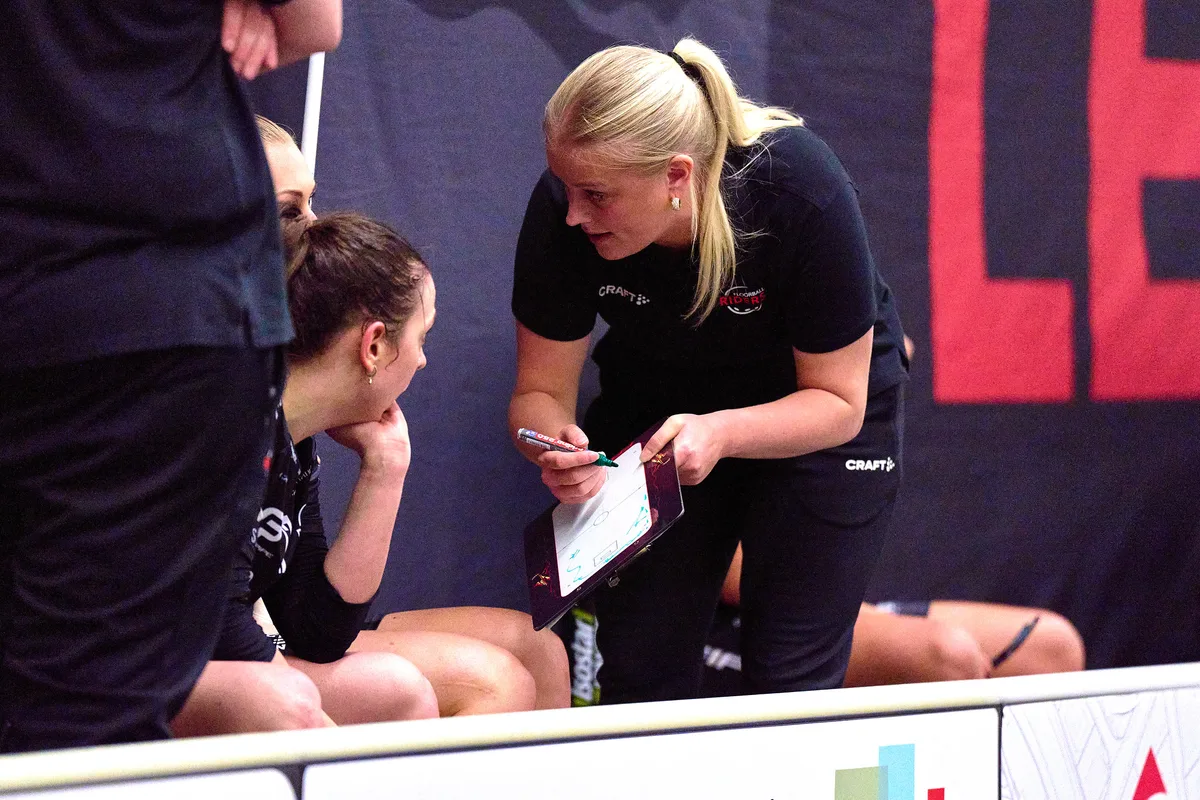 Eine Trainerin mit einem Block beugt sich zu einer Spielerin herunter.