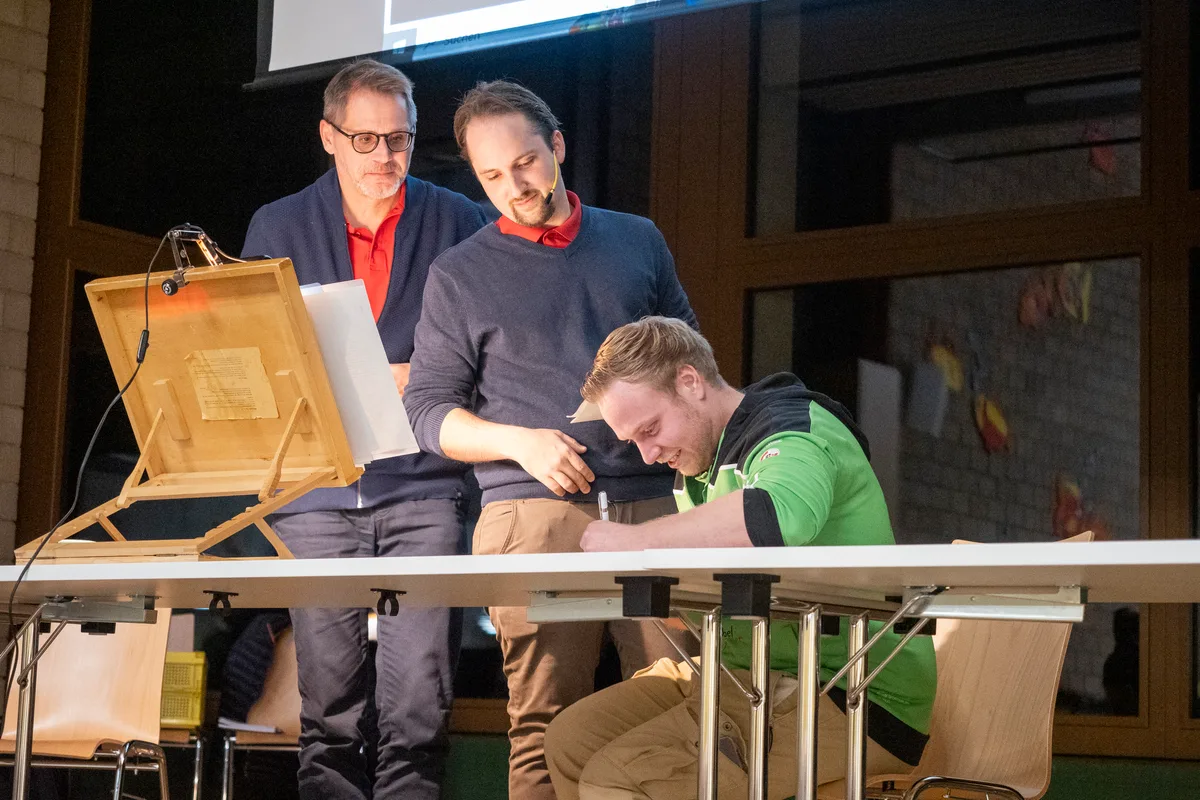 Sportschütze Pascal Bachmann unterschreibt sogleich den Sponsoring-Vertrag, den ihm Gemeindeschreiber Balz Zinniker (links) und Gemeindepräsident Simon Mösch überreicht haben.