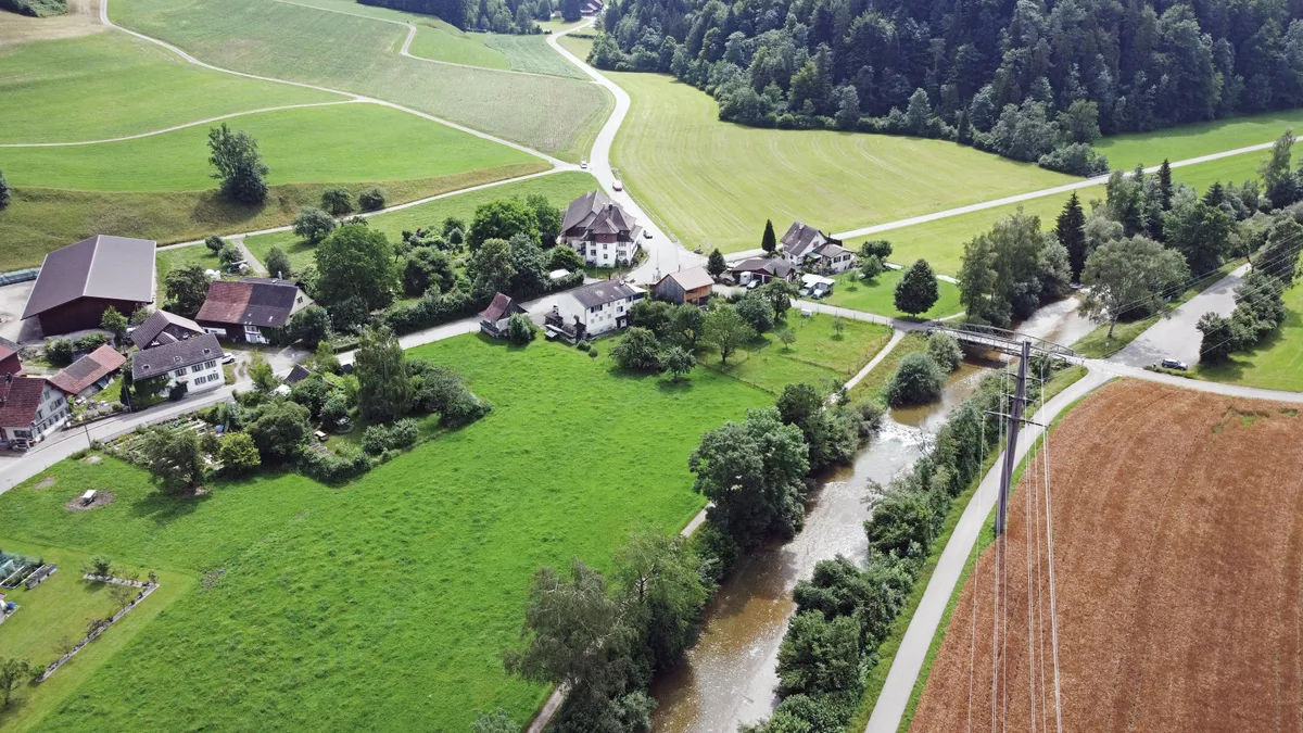Man sieht einen Weiler in einem ländlichen Tal.