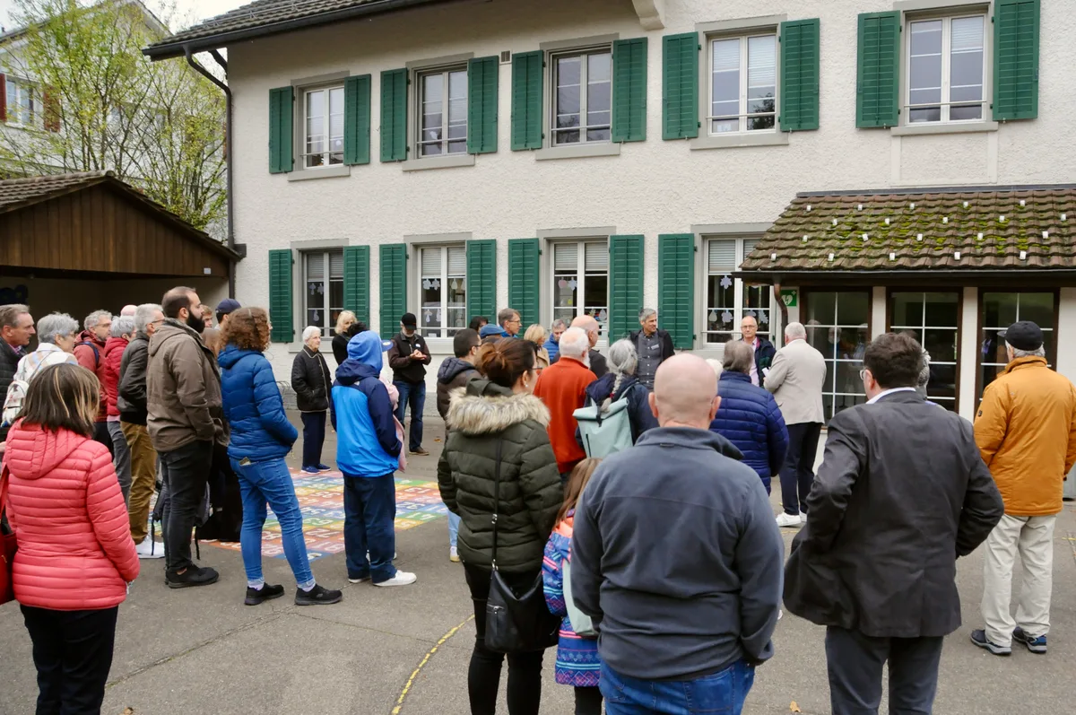 Man sieht Menschen vor einem Schulhaus stehen.