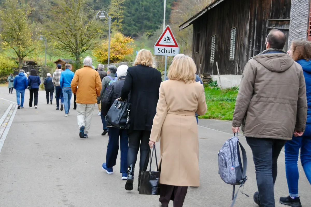 Man sieht Menschen durchs Dorf Richtung Schule spazieren.