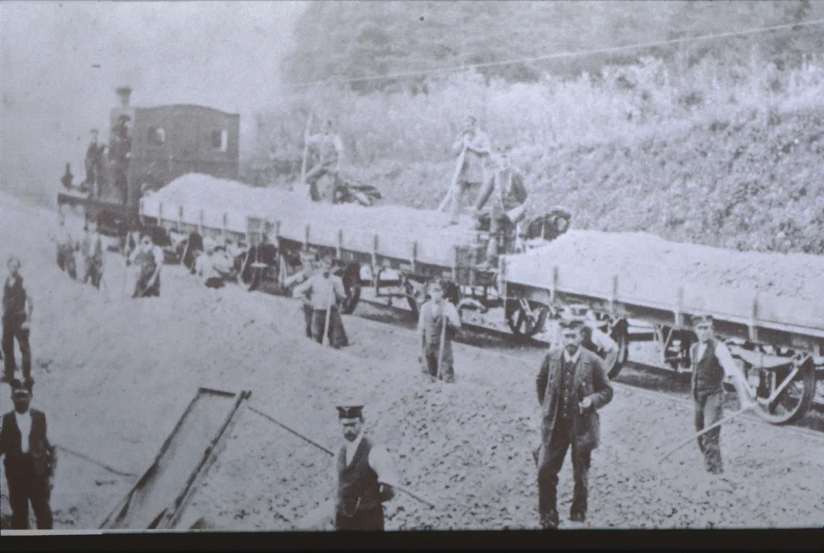 Bahnbau mit Schotterzug: Die Arbeiten verliefen alles andere als reibungslos. Man sieht eine alte Schwarz-Weiss-Aufnahme vom Gleisbau.