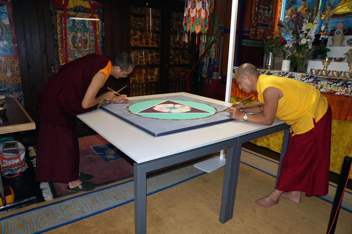 Tenzin Jangchup (links), der Abt des Instituts, und Sonam Gyatso , ganz konzentriert bei der Arbeit. Man sieht zwei Mönche über ein Mandala gebeugt Sand streuen,